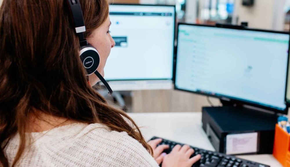 Woman wearing a headset working at a desk with dual computer monitors