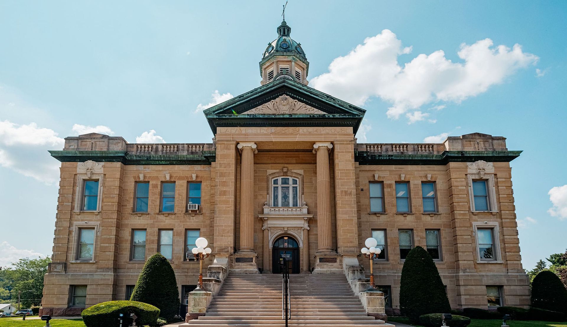 Historic brick courthouse with grand steps, central dome, and blue sky above